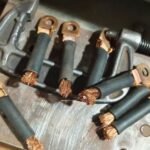 Close-up view of copper wires being soldered together, showing stranded copper conductors with red insulation being joined by silver solder connection in professional electrical work
